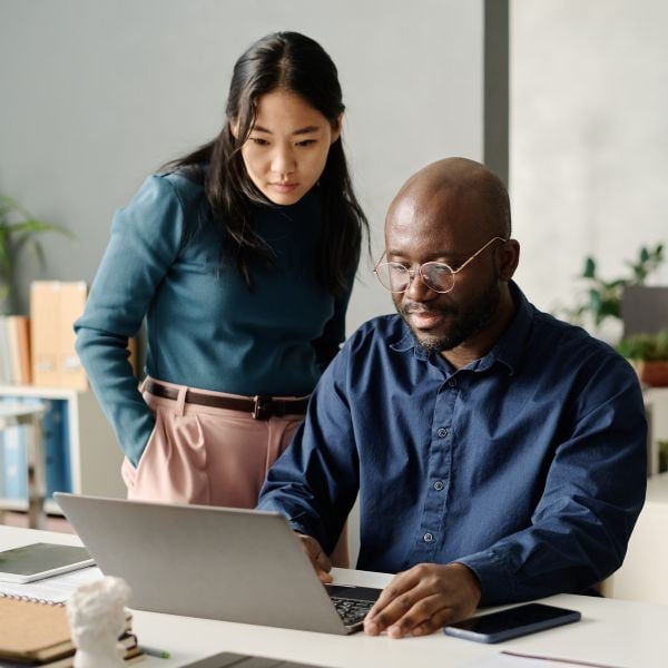 Man working at laptop while woman stands over him and watches