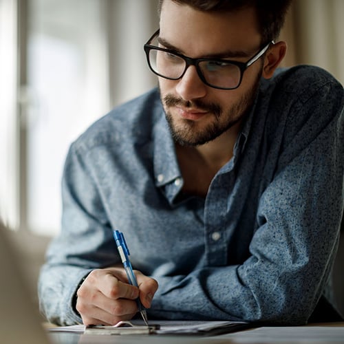 Man with glasses writing on clipboard